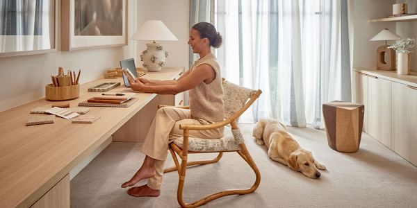Woman working at a desk in a carpeted study with her dog lying beside her