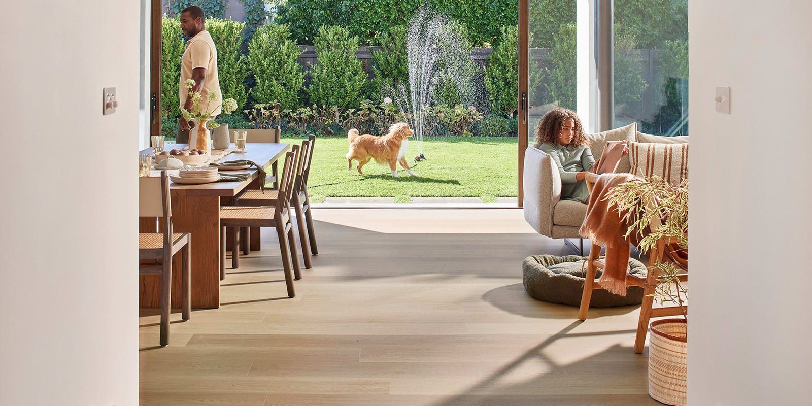 Open-plan living and dining room with light oak floors, a dog running in the garden outside